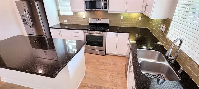 a kitchen with stainless steel appliances granite countertop a refrigerator a sink and white cabinets