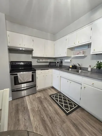 a kitchen with stainless steel appliances granite countertop a stove top oven a sink a dining table and chairs with white cabinets