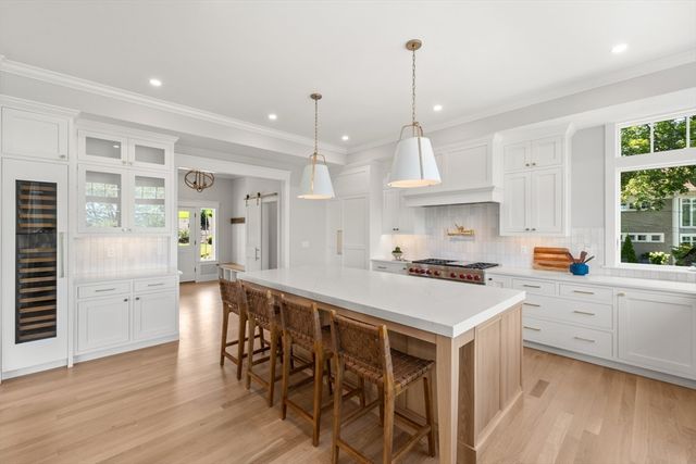 a kitchen with stainless steel appliances a stove a sink a refrigerator white cabinets and wooden floor next to windows