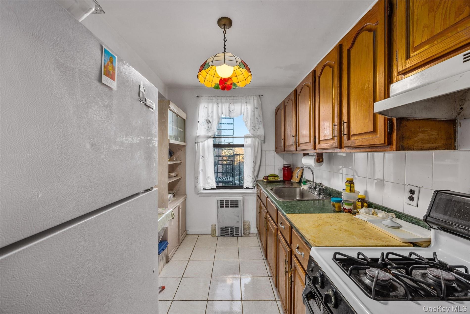 52-35 39th Road, Unit 2C Queens, NY 11377 - Photo 5 of 10 Kitchen with gas range oven, freestanding refrigerator, brown cabinets, hanging light fixtures, and decorative backsplash