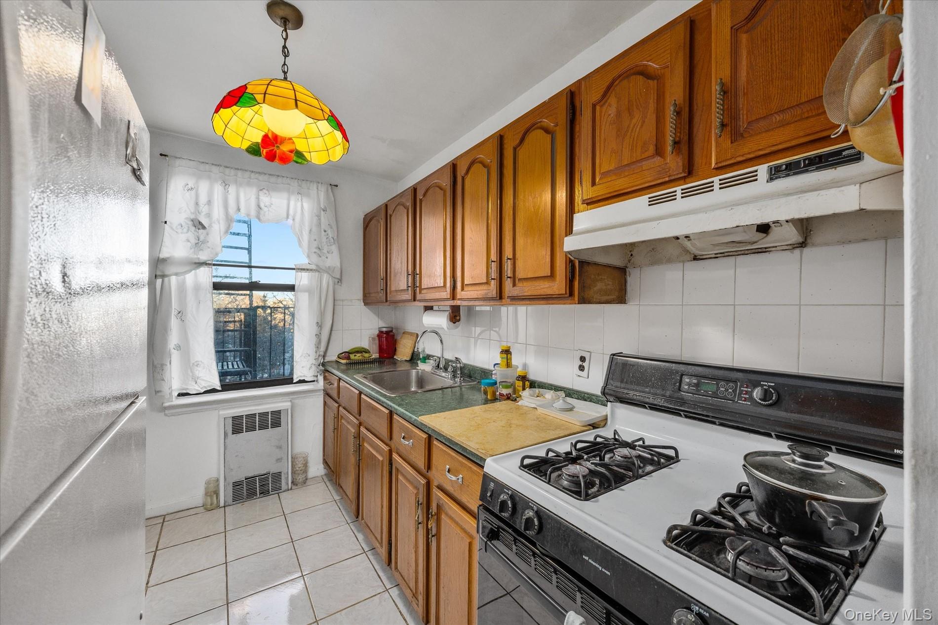 52-35 39th Road, Unit 2C Queens, NY 11377 - Photo 6 of 10 Kitchen with white range with gas stovetop, freestanding refrigerator, tasteful backsplash, and brown cabinetry