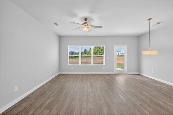 an empty room with wooden floor chandelier fan and windows