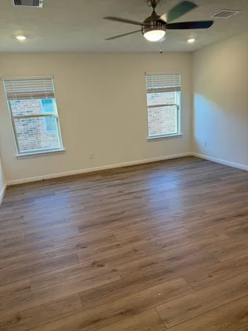 an empty room with wooden floor a ceiling fan and windows