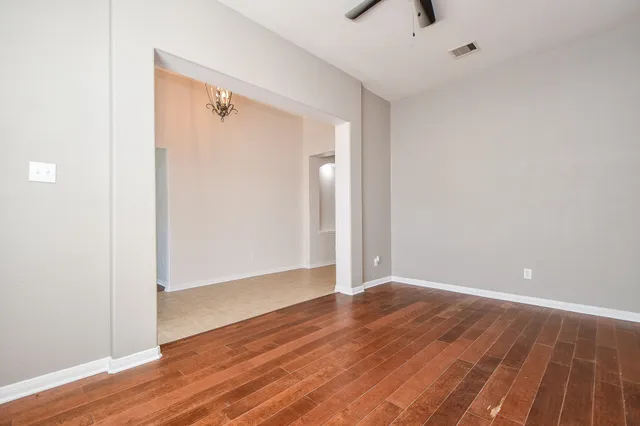 a view of an empty room with wooden floor and a ceiling fan