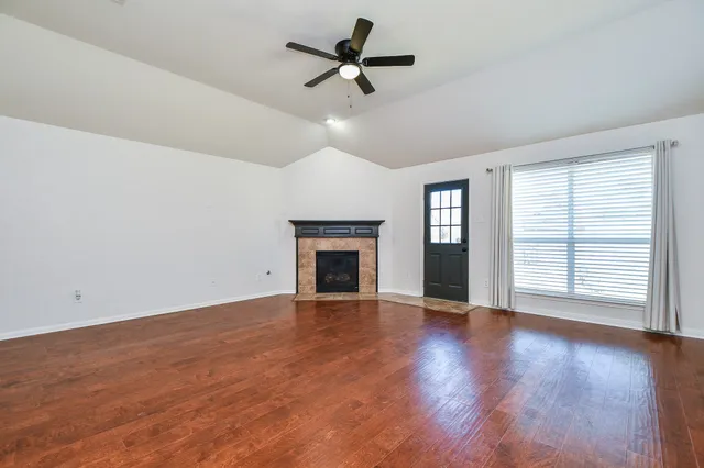a view of an empty room with wooden floor fireplace and a window