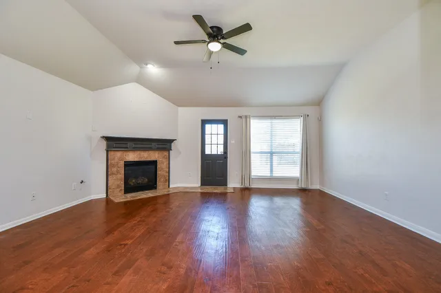 a view of an empty room with wooden floor fireplace and a window