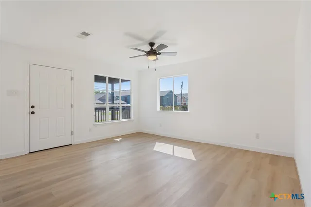 an empty room with wooden floor ceiling fan and windows