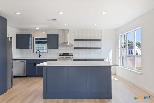 a kitchen with stainless steel appliances granite countertop a sink a stove a refrigerator cabinets and a wooden floor