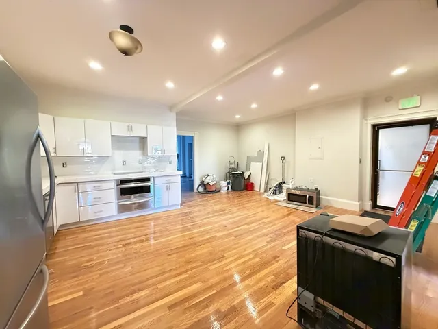 a large kitchen with stainless steel appliances a stove a refrigerator white cabinets and wooden floor