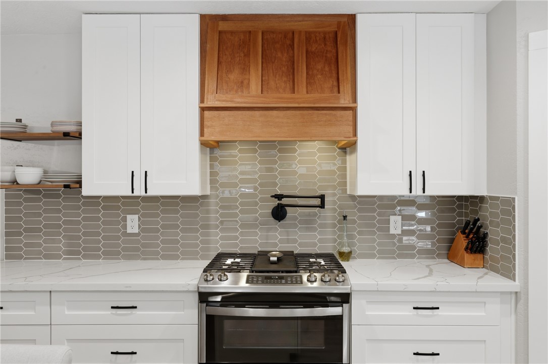 515 Crescent Drive Bryan, TX 77801 - Photo 14 of 43 Kitchen featuring a stainless steel gas range, a wood hood, white shaker cabinetry with black hardware, white countertops with veining, and a gray picket tile backsplash