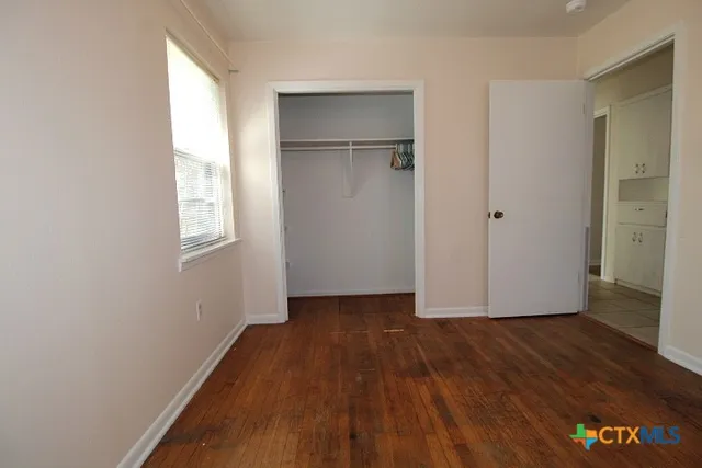 a view of an empty room with wooden floor and a window