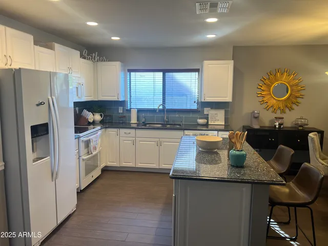 a kitchen with stainless steel appliances granite countertop a sink a stove a refrigerator cabinets and a dining table