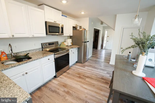 a kitchen with stainless steel appliances a stove top oven a sink a refrigerator white cabinets and wooden floor