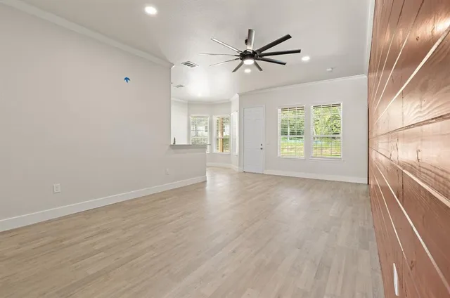 an empty room with wooden floor fan and windows