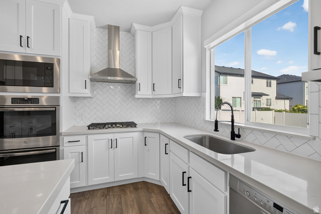 36 West Syracuse Road Vineyard, UT 84059 - Photo 18 of 56 Modern kitchen featuring white shaker cabinetry, stainless steel appliances, a herringbone tile backsplash, an undermount sink with a gooseneck faucet, and wood-finish flooring