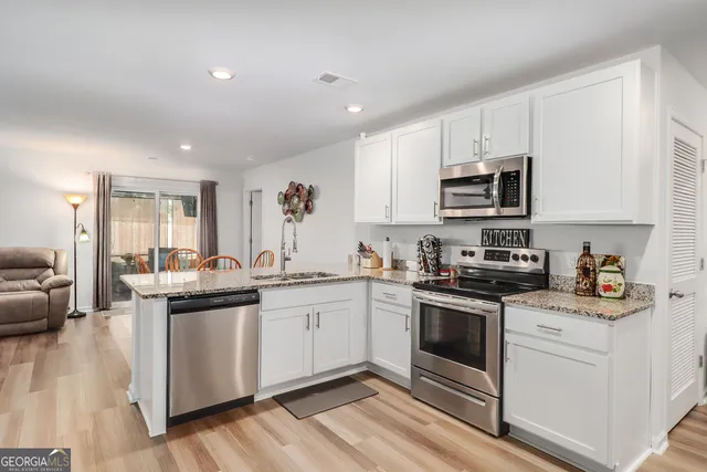 a kitchen with stainless steel appliances granite countertop a stove top oven a sink a refrigerator and white cabinets