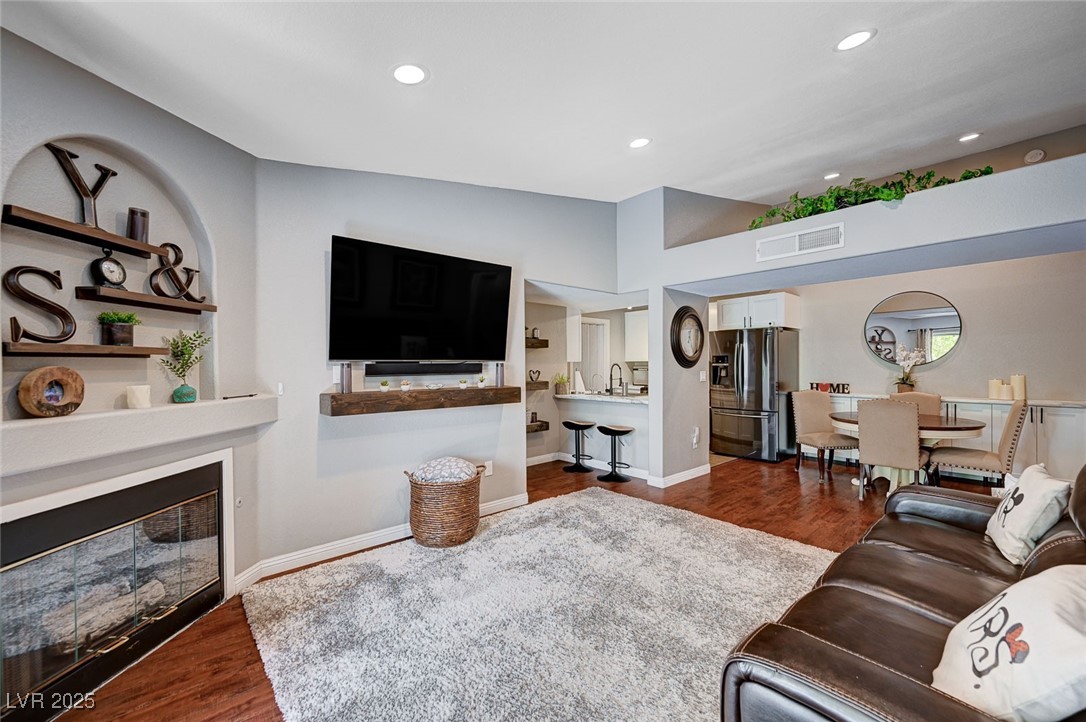 Living room featuring dark wood-style floors, a glass covered fireplace, visible vents, and recessed lighting