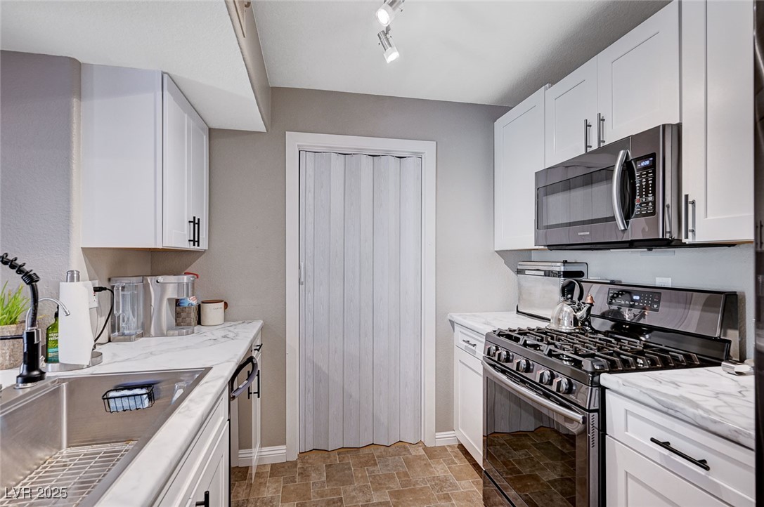 7885 West Flamingo Road, Unit 2023 Las Vegas, NV 89147 - Photo 4 of 34 Kitchen featuring white cabinetry, stone finish floor, stainless steel appliances, and a sink