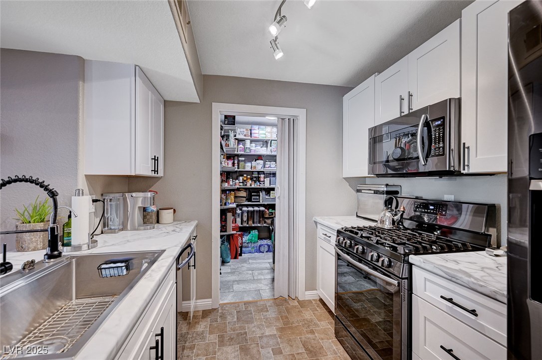 7885 West Flamingo Road, Unit 2023 Las Vegas, NV 89147 - Photo 5 of 34 Kitchen featuring light stone counters, stainless steel appliances, stone finish flooring, white cabinetry, and a sink