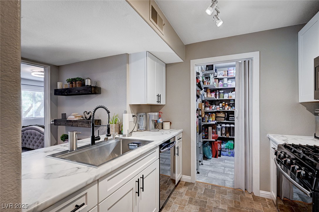7885 West Flamingo Road, Unit 2023 Las Vegas, NV 89147 - Photo 8 of 34 Kitchen with open shelves, visible vents, stone finish flooring, white cabinetry, and a sink