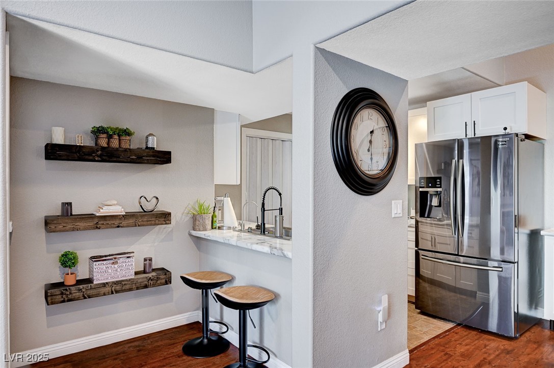 7885 West Flamingo Road, Unit 2023 Las Vegas, NV 89147 - Photo 10 of 34 Kitchen with a breakfast bar area, white cabinetry, a sink, wood finished floors, and stainless steel fridge