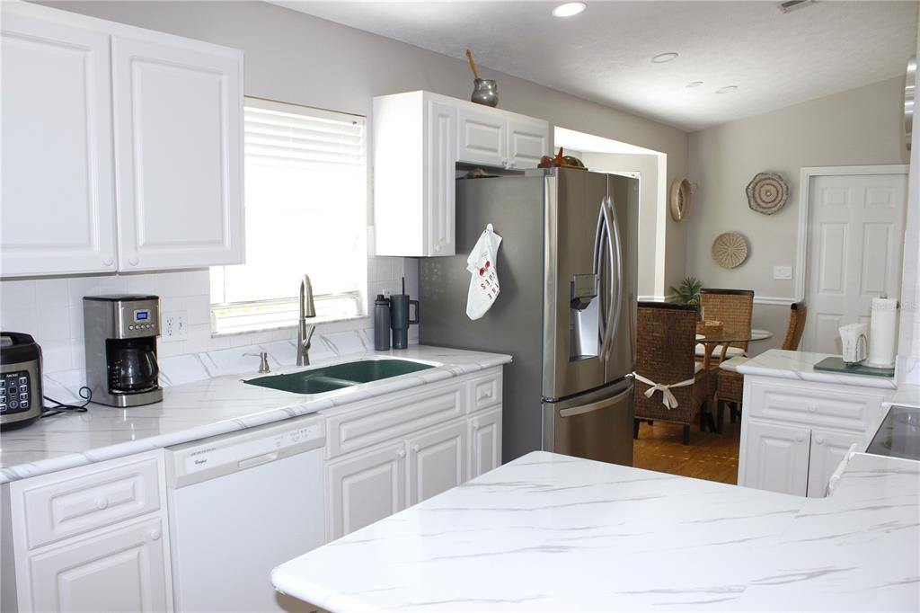 13451 Knotty Lane Hudson, FL 34669 - Photo 9 of 34 a kitchen with stainless steel appliances kitchen island granite countertop a refrigerator a sink dishwasher and white cabinets with wooden floor
