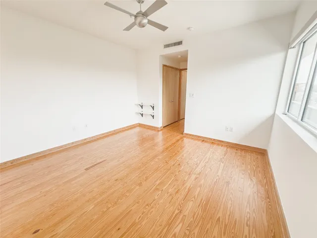 an empty room with wooden floor fan and windows