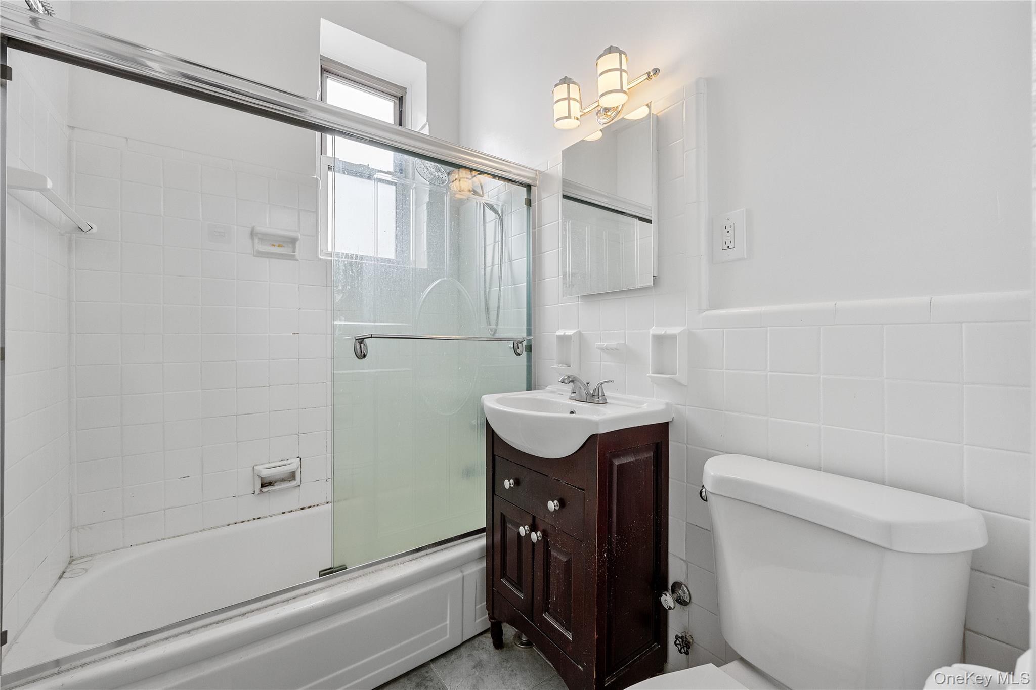 355 Bronx River Road, Unit 1I Yonkers, NY 10704 - Photo 13 of 22 Full bath with vanity, shower / bath combination with glass door, tile walls, and a wainscoted wall