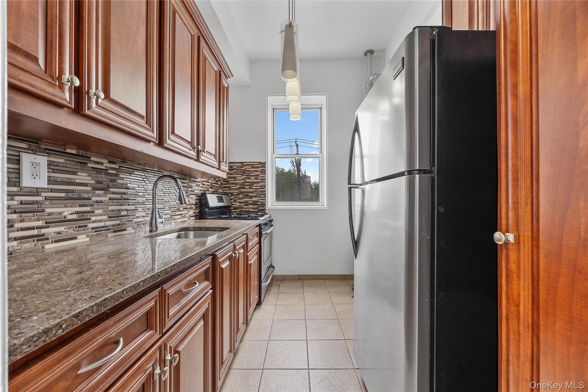 355 Bronx River Road, Unit 1I Yonkers, NY 10704 - Photo 8 of 22 Kitchen with stainless steel appliances, backsplash, dark stone countertops, light tile patterned flooring, and brown cabinetry