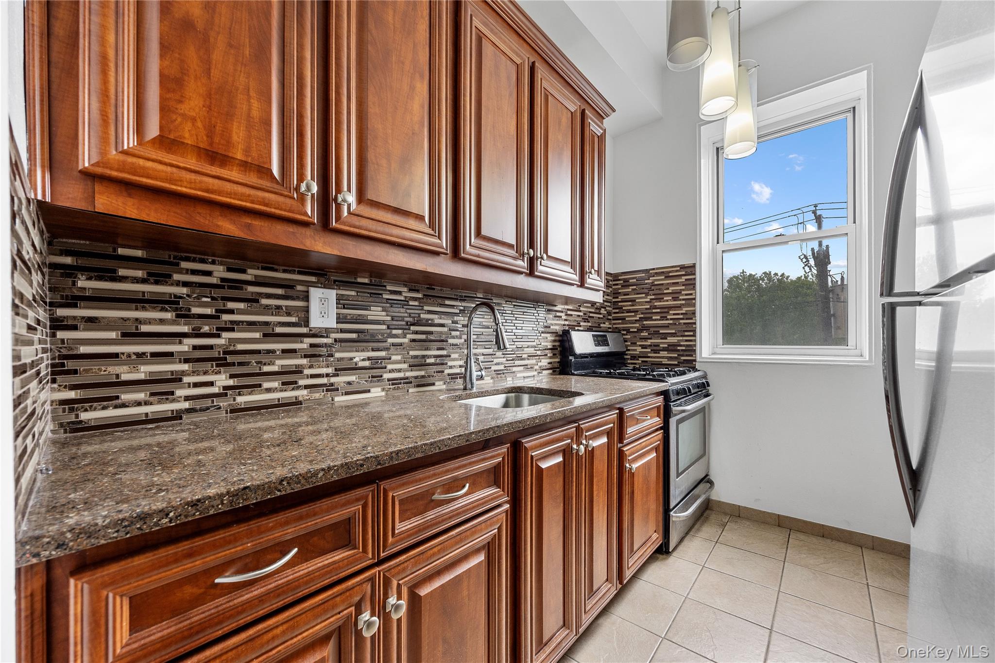 355 Bronx River Road, Unit 1I Yonkers, NY 10704 - Photo 9 of 22 Kitchen with stainless steel appliances, dark stone countertops, light tile patterned floors, backsplash, and hanging light fixtures