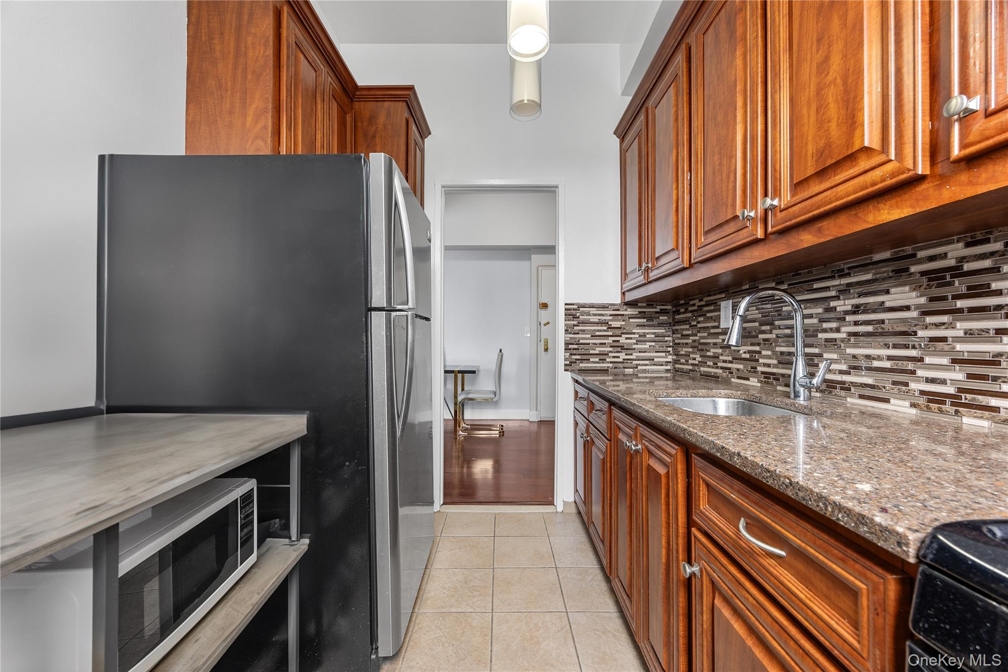 355 Bronx River Road, Unit 1I Yonkers, NY 10704 - Photo 10 of 22 Kitchen featuring appliances with stainless steel finishes, dark stone countertops, backsplash, light tile patterned floors, and brown cabinets