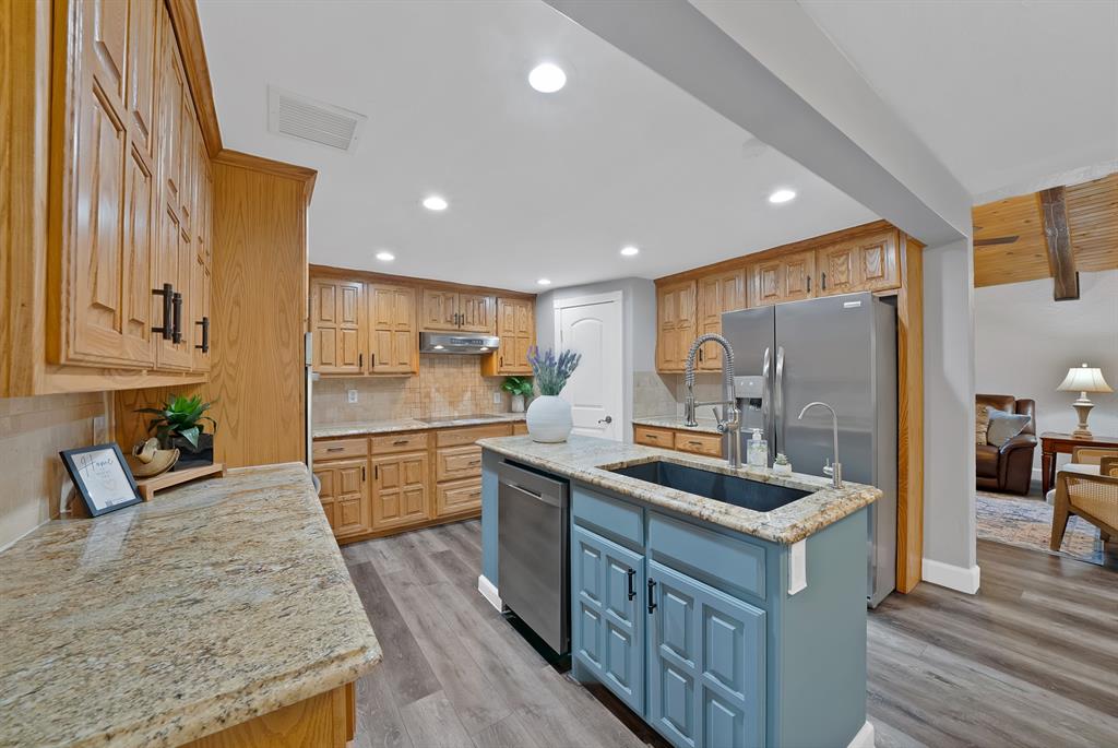 306 Rochelle Boulevard Irving, TX 75062 - Photo 8 of 40 Kitchen featuring wood cabinetry, stainless steel appliances, a center island with sink, granite countertops, and wood-finish flooring