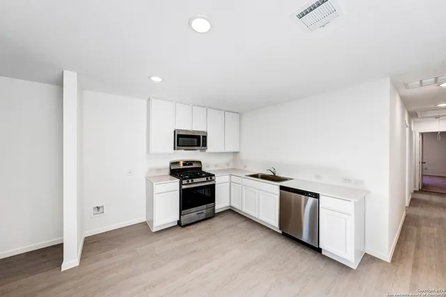 a kitchen with stainless steel appliances a sink a stove a refrigerator and white cabinets