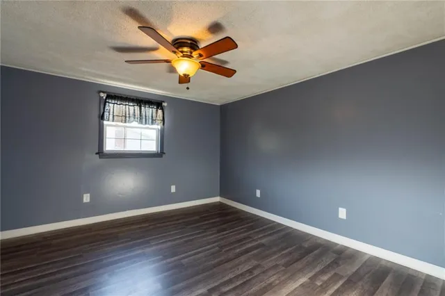an empty room with wooden floor chandelier fan and windows