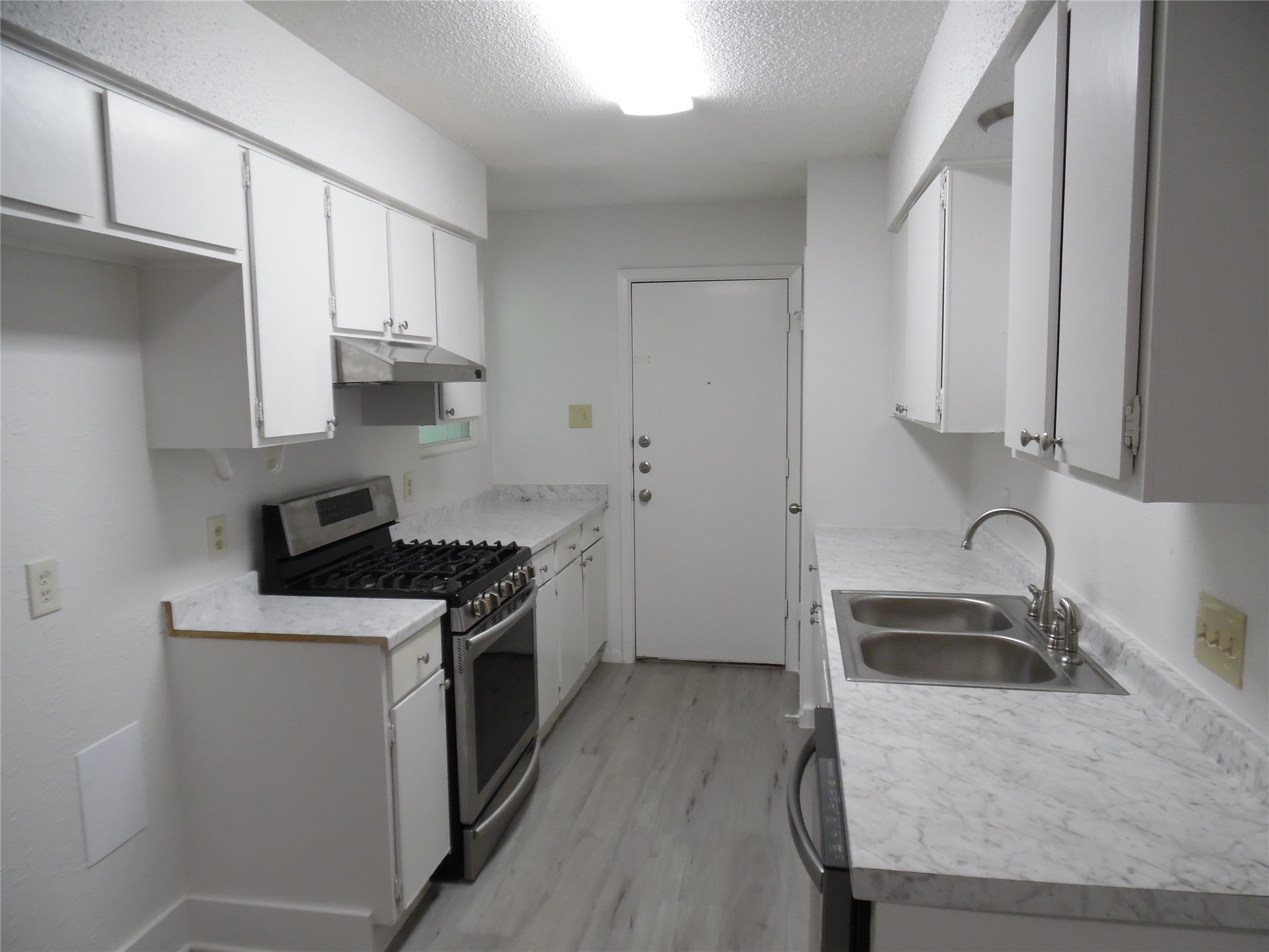 7400 Dixie Drive, Unit B Austin, TX 78744 - Photo 10 of 15 Kitchen featuring white cabinetry, light-toned countertops, a stainless steel gas range, and wood-finish flooring