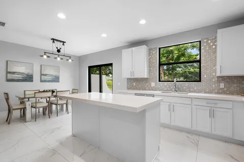a large white kitchen with furniture a sink a window and dining table