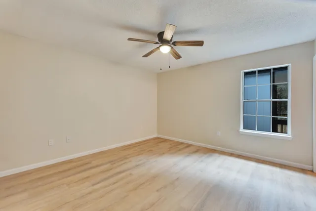 an empty room with wooden floor ceiling fan and windows