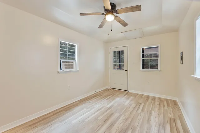 an empty room with wooden floor ceiling fan and windows