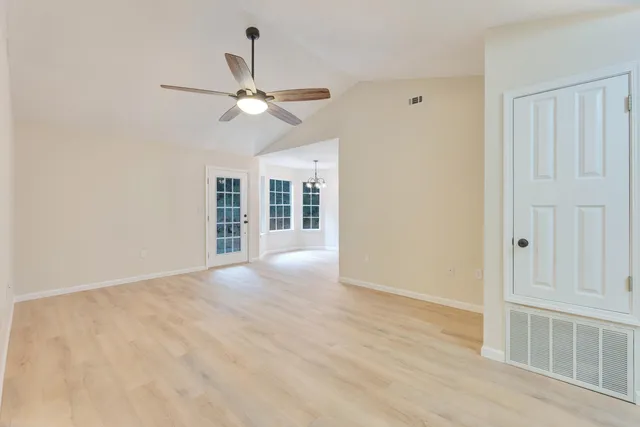 an empty room with wooden floor ceiling fan and windows