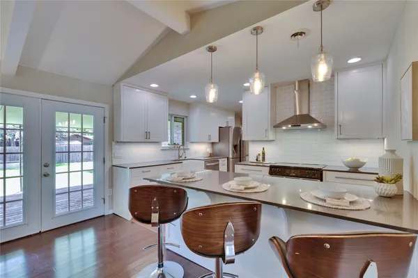 a kitchen with stainless steel appliances granite countertop a sink a refrigerator a stove a dining table and chairs with wooden floor