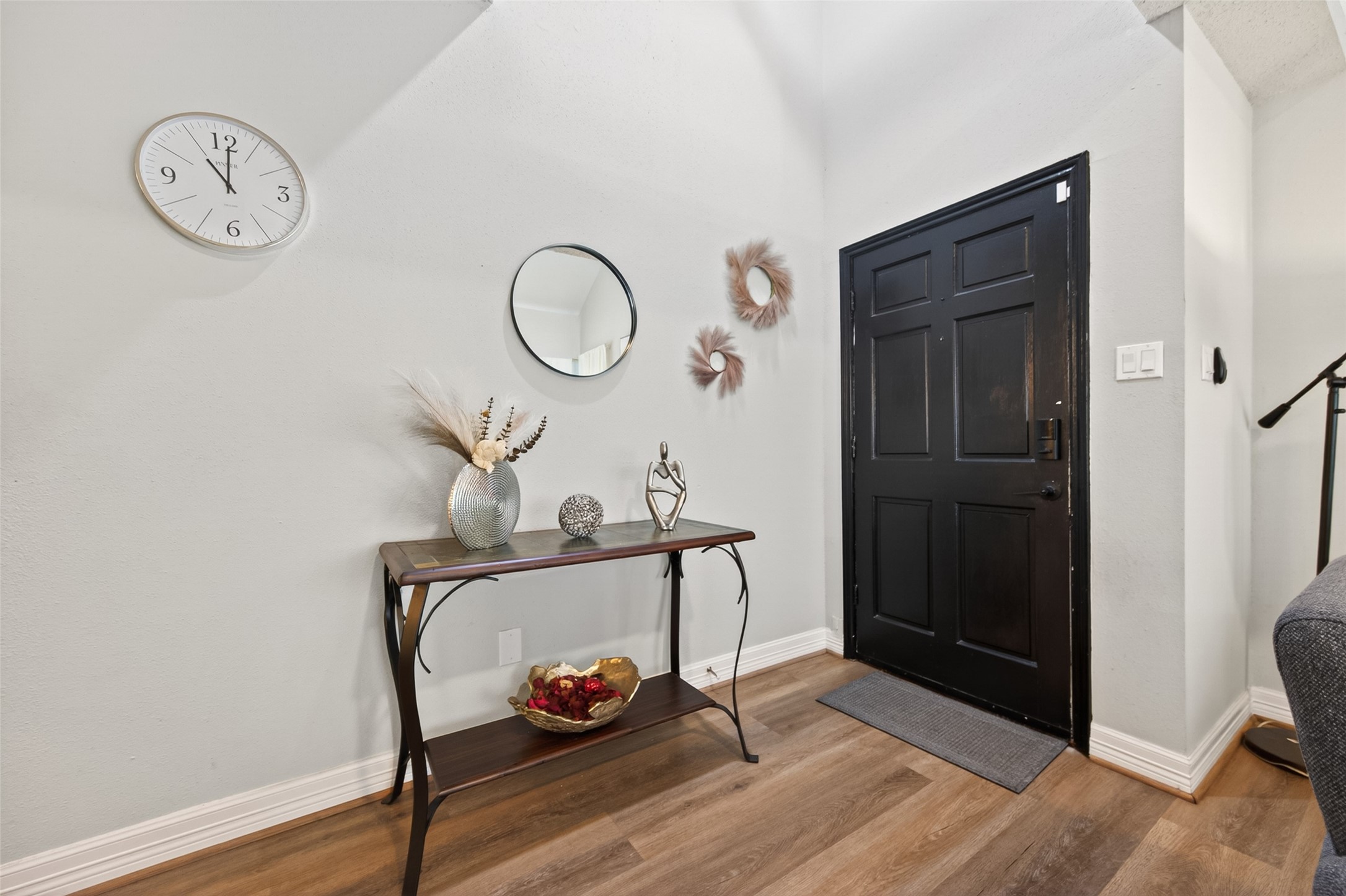 18446 North Willow Bluff Road Katy, TX 77449 - Photo 5 of 33 Bright entryway with a sleek black door, neutral walls, and wood flooring. Features a stylish console table with decorative items, a wall clock, and a mirror for a welcoming touch.