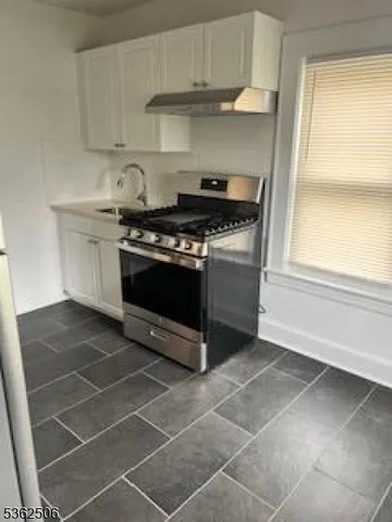 a kitchen with granite countertop a stove a sink and a white cabinets