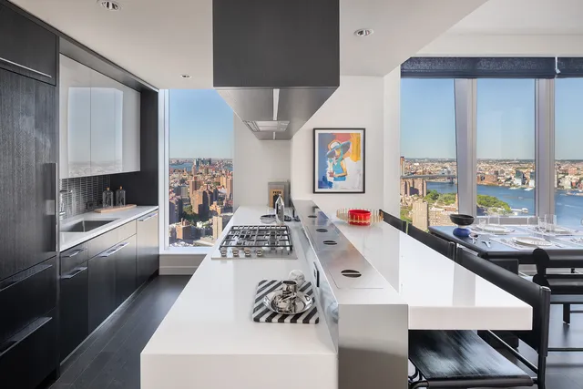a living room with stainless steel appliances furniture a large window and a kitchen view