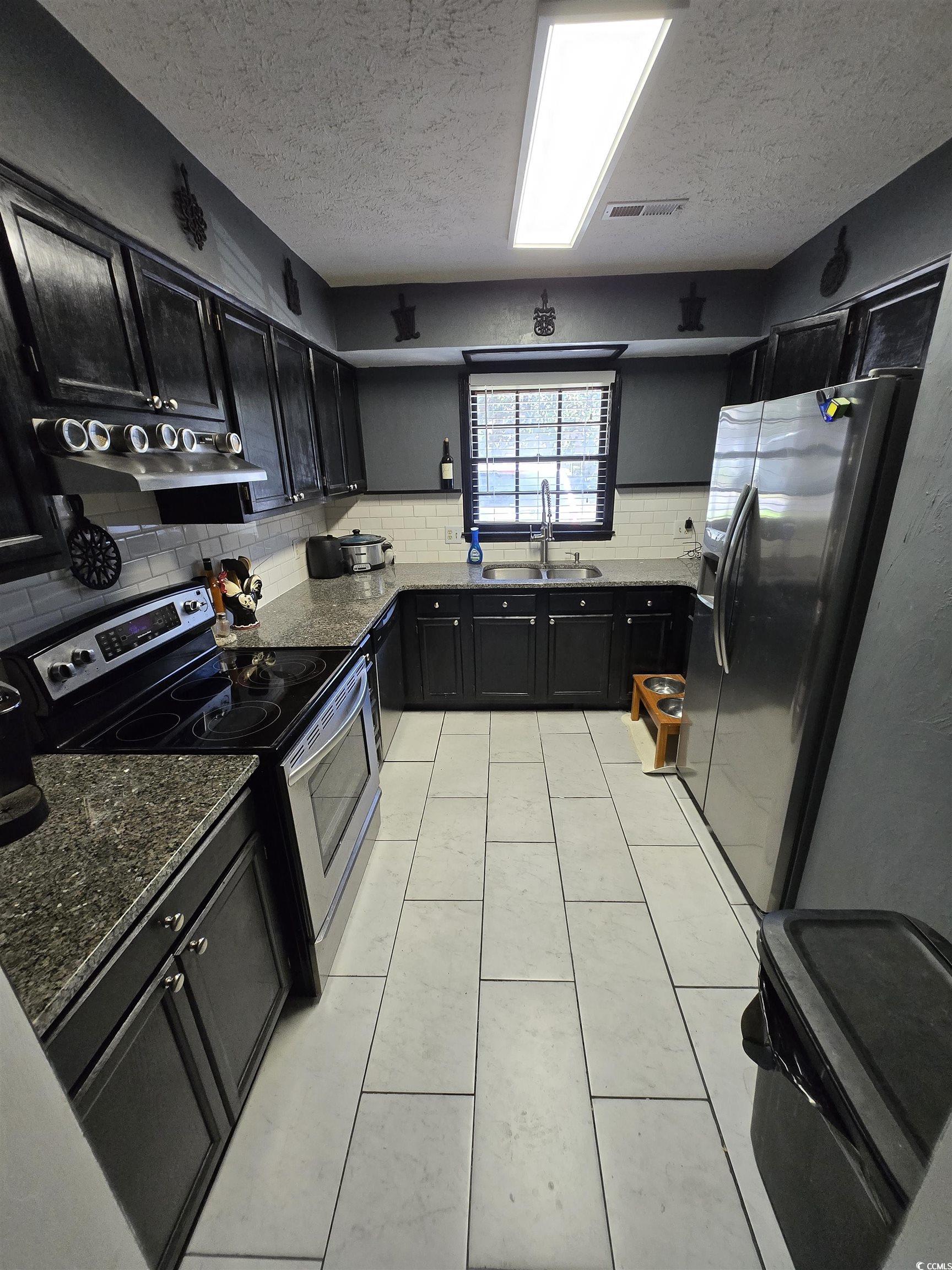 830 44th Avenue North Myrtle Beach, SC 29577 - Photo 4 of 13 Kitchen with dark cabinets, appliances with stainless steel finishes, dark stone counters, a textured ceiling, and light tile patterned floors