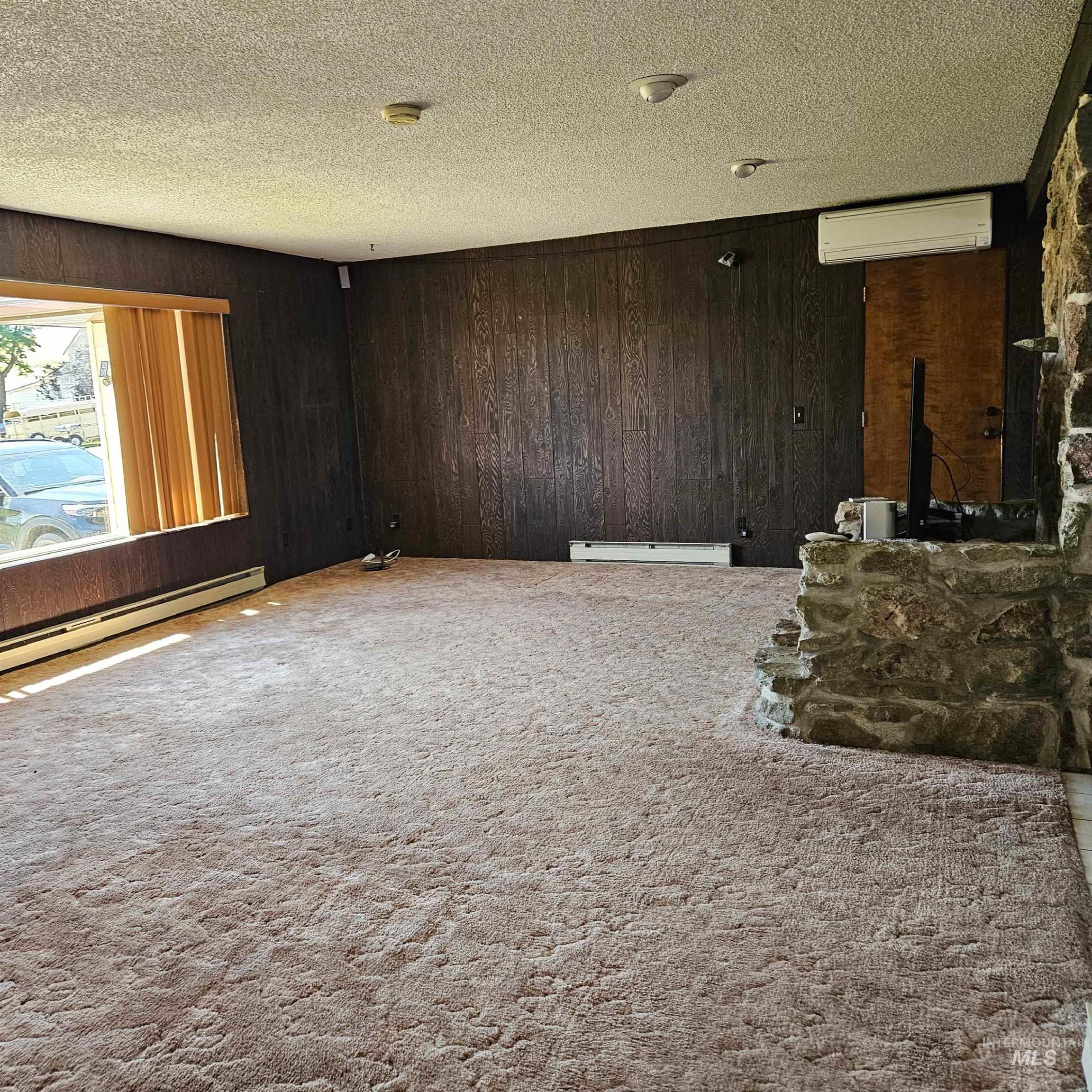 1034 Greencreek Road Greencreek, ID 83533 - Photo 5 of 42 Unfurnished living room with wooden walls, carpet flooring, a textured ceiling, a wall mounted air conditioner, and baseboard heating