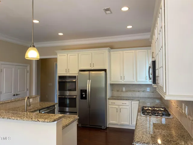 a kitchen with granite countertop stainless steel appliances a refrigerator a stove cabinets and living room view