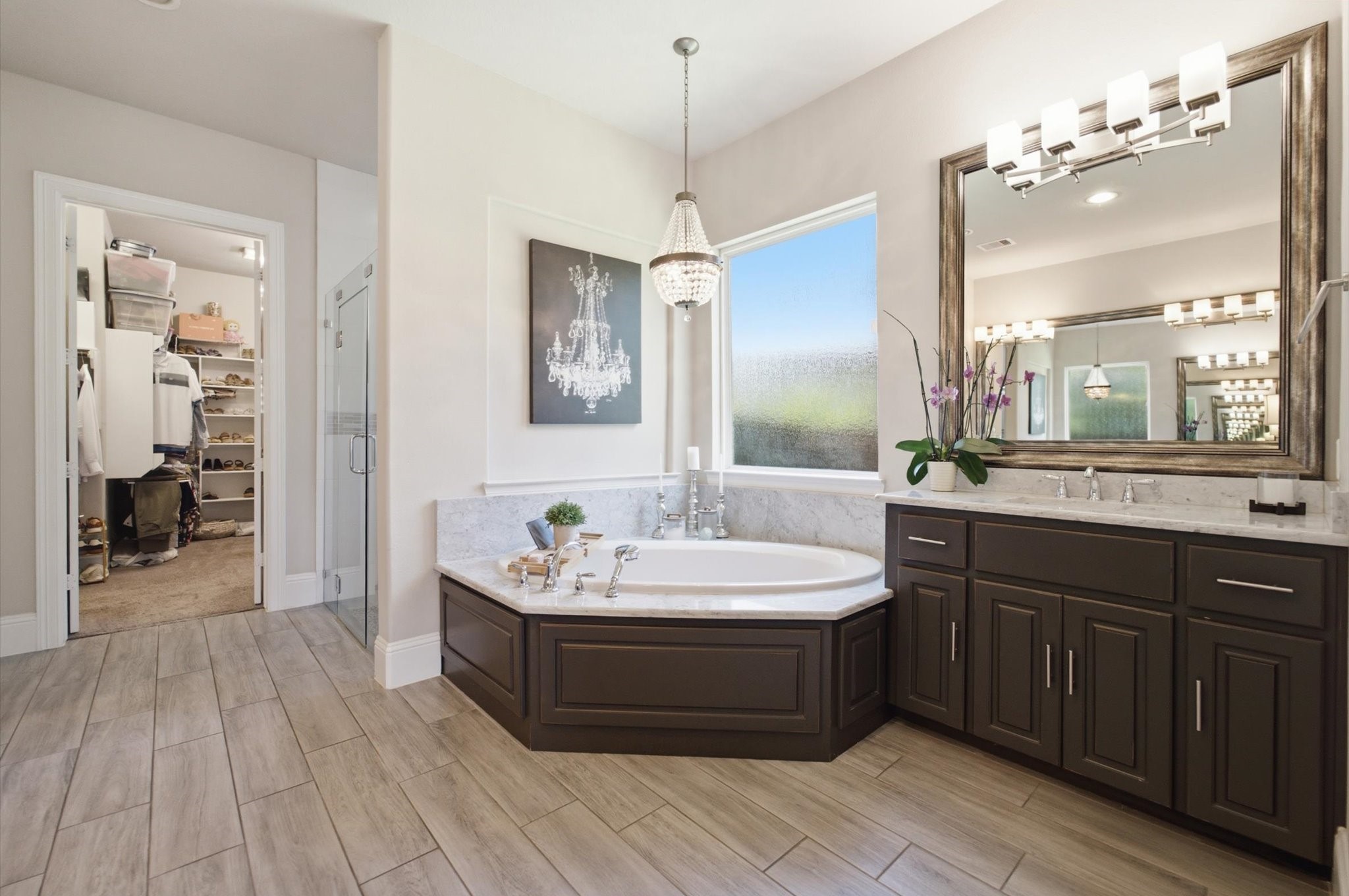 23722 Thortons Park Lane Spring, TX 77389 - Photo 14 of 48 This elegant bathroom features a large soaking tub, spacious vanity with dual sinks, and a modern light fixture. The room has a neutral color palette and wood-style flooring, with a walk-in closet and glass-enclosed shower nearby. A large window provides natural light, enhancing the open feel.
