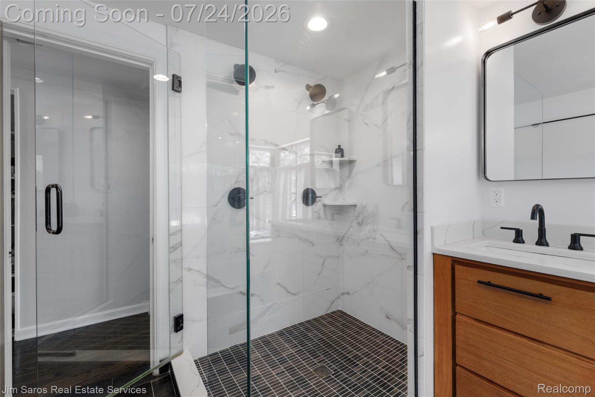 757 Middlesex Road Grosse Pointe, MI 48230 - Photo 28 of 45 Full bathroom featuring a frameless glass shower enclosure, white marble-look tile walls, black grid shower floor tile, a natural wood-finish vanity with a white countertop, and a matte black faucet