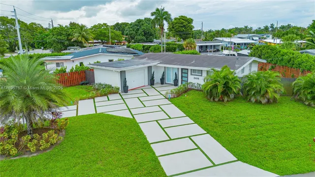 a view of a white house with a yard plants and large tree