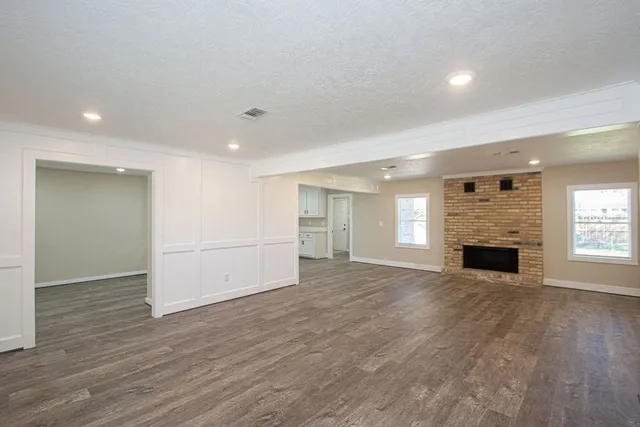 an empty room with wooden floor fireplace and windows